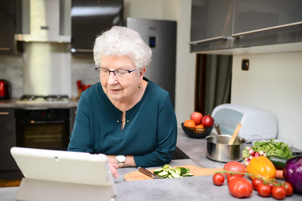 happy senior active woman cooking at home in modern kitchen and looking for recipe on internet computer tablet